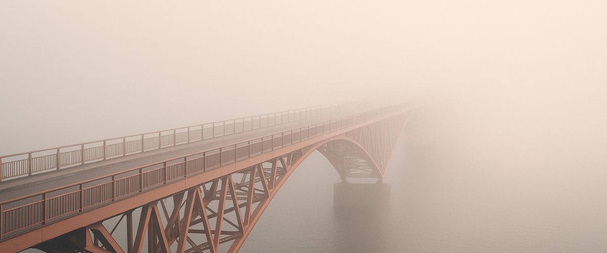 Lange Brücke im Nebel, kaum sichtbares Ziel – Sinnbild für Unsicherheit und Systemdruck